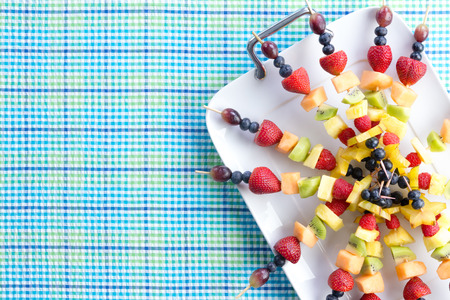 Fresh healthy tropical fruit shish kebabs arranged neatly on a tray placed on a picnic table with a...