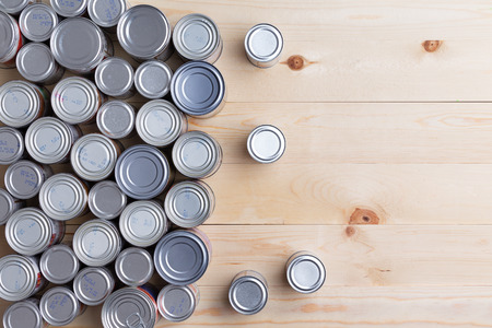 Conceptual background of multiple canned foods in sealed aluminum tins or cans of varying sizes arranged on a wooden table with copy space, overhead viewの写真素材