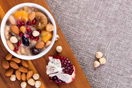 Noah's food or ashure, a speciality Turkish sweet grain pudding, served with hazelnuts, almonds and pomegranate seeds, overhead view with ingredients and copy space on textured beige linenの写真素材