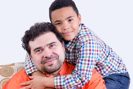 Cheerful child in checkered shirt with grin hugging his smiling father with beard from behindの写真素材