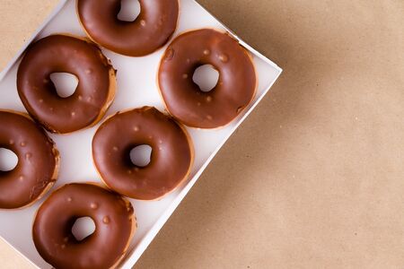 First person perspective top down view of six chocolate and cream donuts in open box over brown table with copy spaceの写真素材