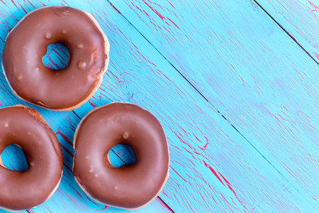 Three crispy cream filled chocolate ring donuts topped with chocolate icing on a rustic turquoise blue wooden background with copy spaceの写真素材