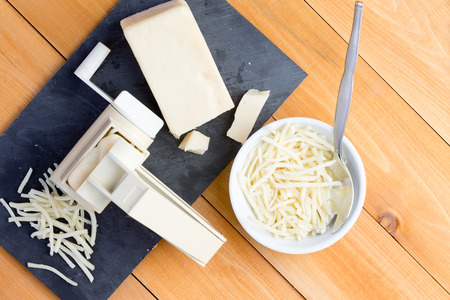 Preparing grated gruyere cheese for cooking with an overhead view of a rotary grater and wedge of...