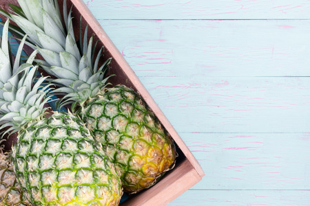 Fresh pineapples in a wooden crate displayed at an angle on a blue painted wooden table with copy space, overhead viewの写真素材