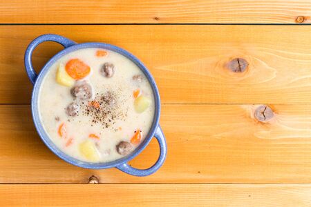 Nutritious meatball soup with vegetables garnished with ground black pepper and served in a blue bowl on a natural wood table with copy space, overhead viewの写真素材