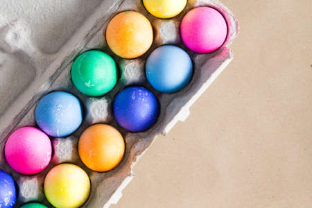 Vibrant hand dyed colorful Easter eggs in a cardboard egg box viewed from above on a beige background with copy space for your greetingの写真素材