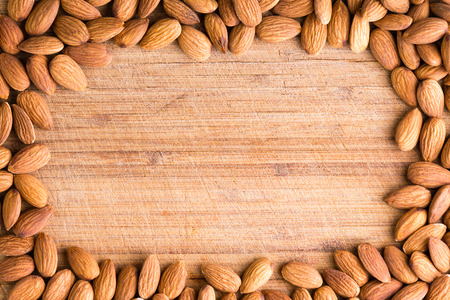 Rectangular border or frame of fresh raw almonds rich in vitamin e, protein and dietary fiber arranged around an old wooden cutting board with central copy spaceの写真素材