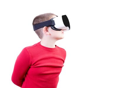 Boy in red long sleeved shirt wearing virtual reality glasses with arms folded behind his back peers...