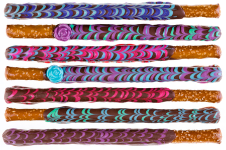 Row of seven colorfully decorated chocolate covered pretzel sticks on a white backgroundの写真素材