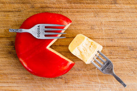 Creative arrangement of wax covered cheese wheel with one quarter cut from it and a fork with cheese...