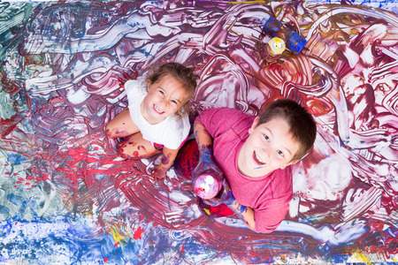 Happy girl and boy looking up while partially covered in paint from mural they are making with their handsの写真素材