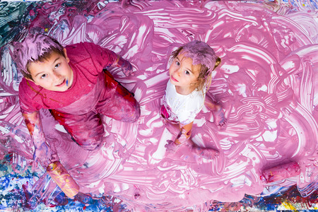 Happy girl and boy pausing from their work while partially covered in paint from mural they are making with their handsの写真素材
