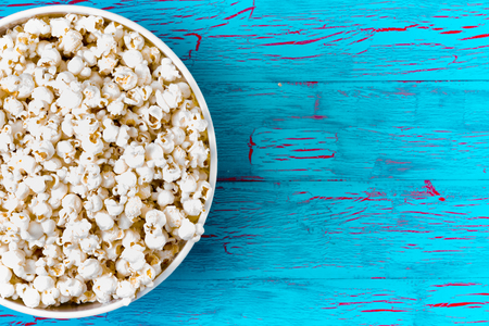 Bowl of freshly made popcorn on a colorful blue crackle paint picnic table as a summer snack, overhead view with copy spaceの写真素材