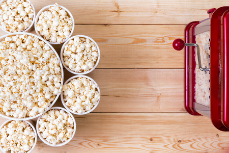 Dishes of fresh popcorn arranged in a decorative circle around a larger center bowl alongside a machine on a wooden table with copy spaceの写真素材