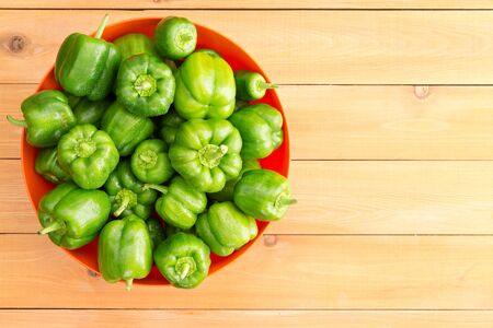 Overhead view of large red bowl filled beautiful fresh green peppers against a wooden backgroundの写真素材
