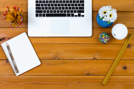 Clean desk with neatly arranged office supplies including a laptop, notepad and pencil, flowers, paperweight, ruler and takeaway coffee around central copy space, view from aboveの写真素材