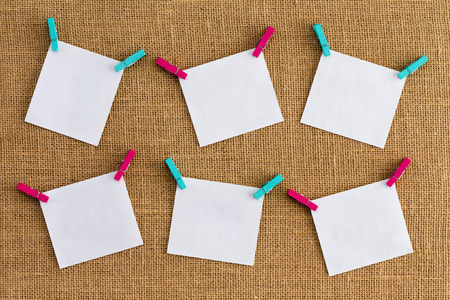 Six misaligned blank white notepads on hessian or burlap fabric hanging from alternating colorful...