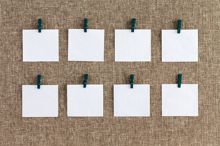 Precisely aligned rows of blank memo pads hanging from wooden clothes pegs over a textured woven...