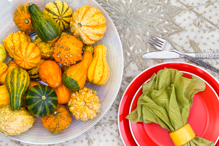 Colorful Thanksgiving centerpiece with ornamental gourds in different colors of orange and green alongside a matching place setting with orange plate and green napkin, overhead viewの写真素材
