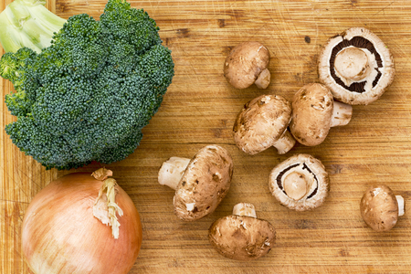 Top down view on raw mushrooms, broccoli and onion ready to be prepared over wooden cutting boardの写真素材