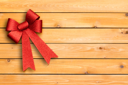 Stylish festive red Christmas ribbon arranged neatly in the corner of a cedar wood board background with copy space on decorative woodgrain and knotsの写真素材