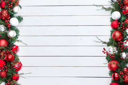 Double sided festive red and silver baubles in a Christmas border with fresh foliage and berries over rustic white stained wood with copy spaceの写真素材