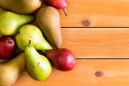 Pile of delicious raw brown, green and red pears on wooden surface with copy space on opposite side