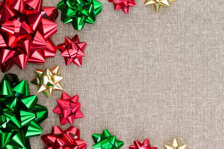 Colorful Christmas foil bow background on burlap with a neat symmetrical arrangement in different sizes as a side border on the textured hessian textile with copy spaceの写真素材