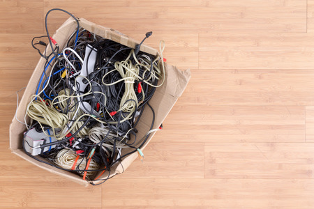 Old battered cardboard box with electrical cords and connectors for electronic devices on a wooden background with copy space viewed from aboveの写真素材