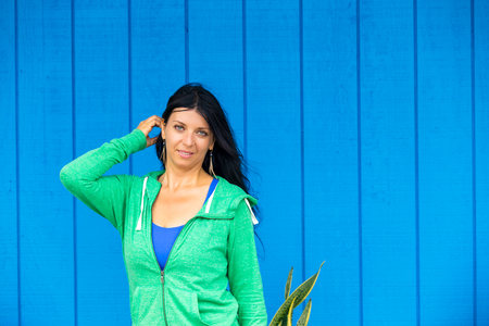 Pretty young woman with her hand raised to her long dark hair posing in front of a bright blue wooden wall with copy space on Oahu, Hawaiiの写真素材