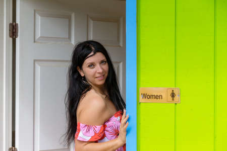 Pretty smiling seductive woman in an entrance door to a brightly colored green restroom facility in a park on Oahu, Hawaiiの写真素材