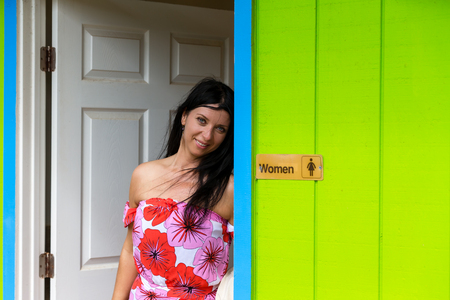 Pretty young woman leaning against a restroom door in a colorful bright green ablution hut in a park in Oahu, Hawaii smiling at the cameraの写真素材