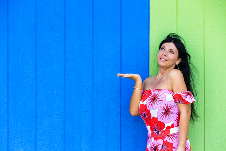 Young woman looking at her empty extended hand ready for your product placement as she poses against a wooden wall in tropical blue and green with copy spaceの写真素材