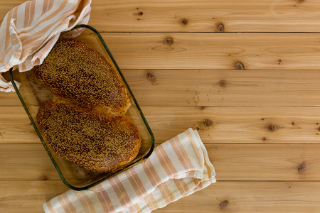 Loaves of newly baked healthy wholegrain bread in a glass oven dish with striped kitchen cloths on a wooden background with copy space viewed from aboveの写真素材