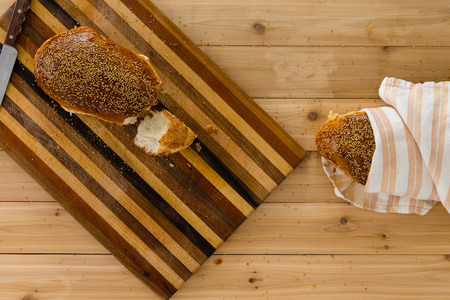 Homemade fresh crusty wholewheat bread with one loaf on a decorative bread board and a second wrapped in a cloth viewed from above on a wooden tableの写真素材
