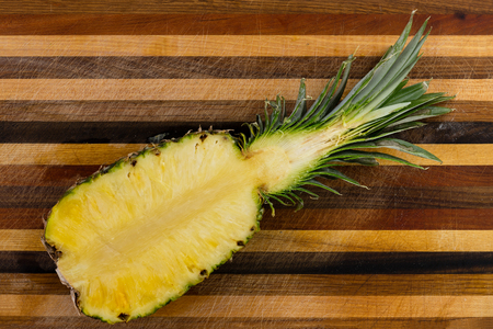 High-angle view close-up of the cross section of a fresh and nutritious pineapple on a striped wooden cutting boardの写真素材