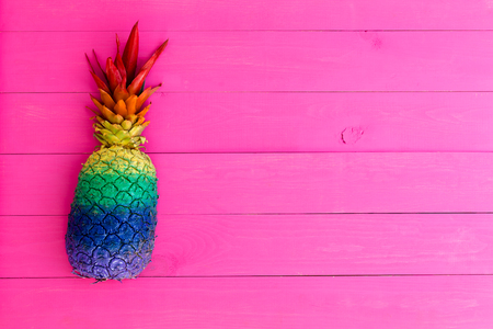 Colorful pineapple painted with rainbow stripes as a side border on a bright vivid pink wooden background with copy spaceの写真素材