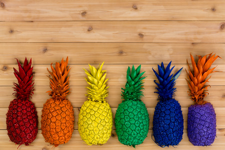 Colorful row of painted rainbow colored tropical pineapples forming a bottom border over a knotty hardwood background with copy spaceの写真素材