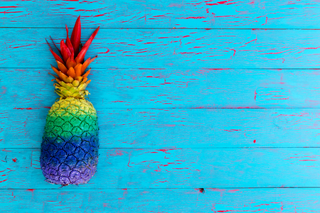 High-angle close-up view of a whole pineapple painted in stripes of vivid colors on a rustic blue wooden tableの写真素材