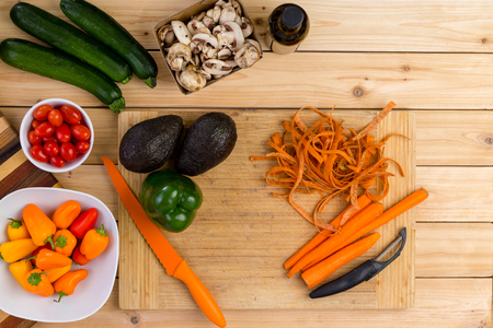 Fresh vegetable ingredients on a kitchen table with a peeler and knife including avocado, peppers, carrots, tomato, zucchini and mushroomsの写真素材