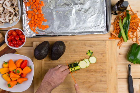 Chef slicing a fresh zucchini or courgette with a sharp kitchen knife as he prepares an assortment of fresh vegetables for cooking viewed from aboveの写真素材