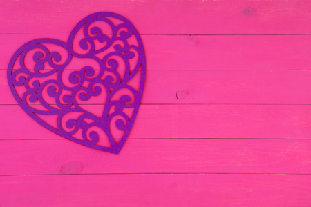 Decorative purple filigree heart on an exotic bright pink wooden background with copy space for a Valentines or anniversary greetingの写真素材