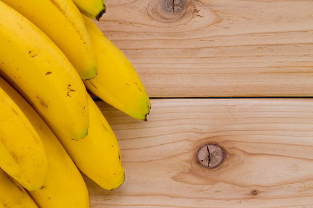 Side border of a bunch of ripe yellow tropical bananas over a wooden background with knots and copy spaceの写真素材
