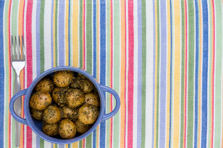 Pot of savory seasoned baby potatoes with herbs and spices on a colorful striped place mat or tablecloth with a fork and copy spaceの写真素材