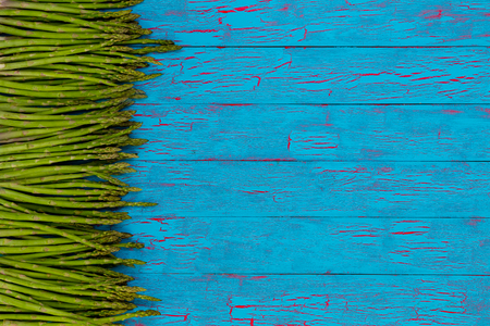 Side border of fresh green asparagus spears, tips or shoots on colorful blue crackle paint wood with copy spaceの写真素材