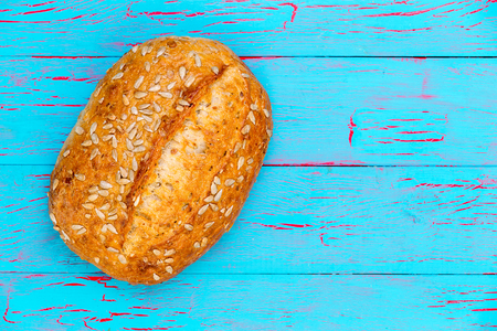 Freshly baked crusty bread roll with sunflower seeds placed to the side over a blue crackle painted wooden background with copy space in an overhead viewの写真素材