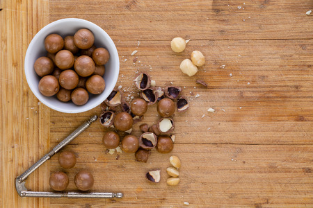Shelling fresh macadamia nuts for eating or cooking in an overhead view of whole nuts, cracked shells and a nutcracker on a wooden bamboo board with copy spaceの写真素材