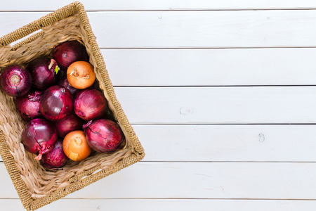 Rustic wicker basket with a mix of healthy fresh red and brown onions viewed from above on a white wood background with copy spaceの写真素材