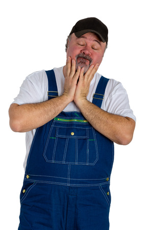 Helpless man wearing dungarees with cap standing against white backgroundの写真素材