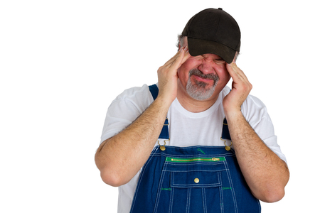 Workman in bib overalls with a migraine headache grimacing with the acute pain as he rubs his temples with his fingertips in a healthcare and medical concept over whiteの写真素材